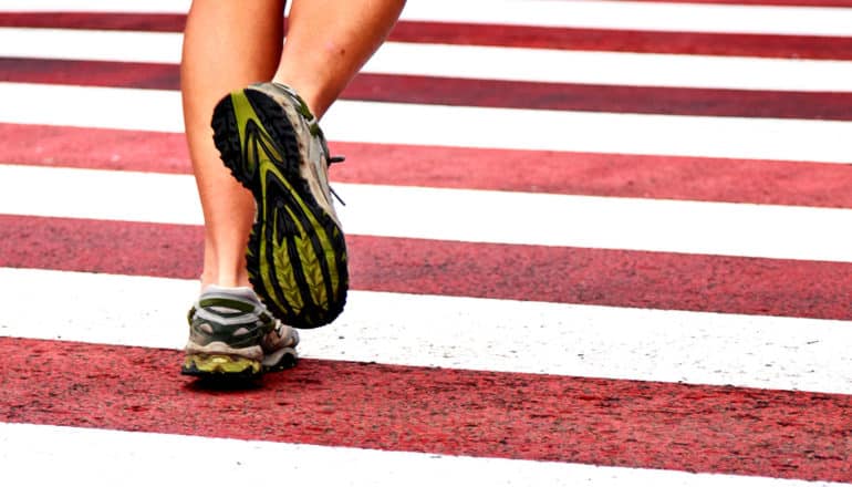 A person runs on a red and white crosswalk, with their lower legs and running shoes visible