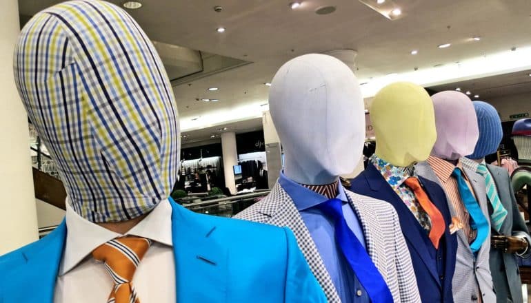 Mannequins wearing different colored suits and ties also have different colored cloth over their faces, masking their features