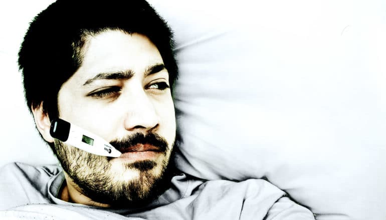 A man lays in bed with a thermometer in his mouth