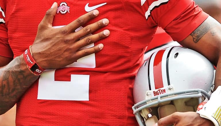 A football player holds his hand over his heart and his helmet under his other arm