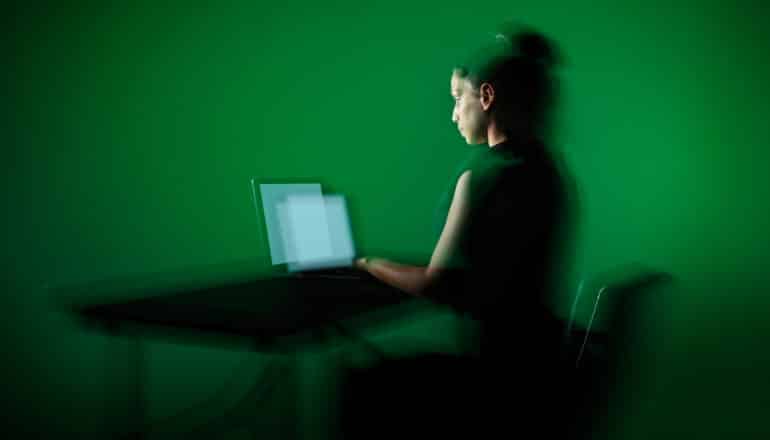 blurry, green-tinted image of person at laptop