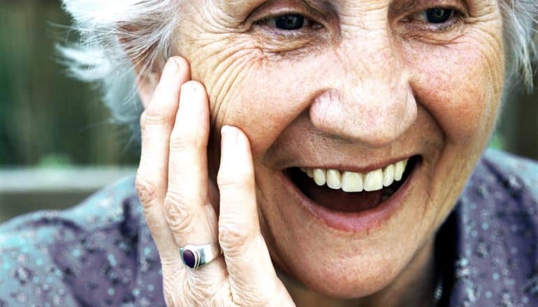 An older woman laughs and touches her face