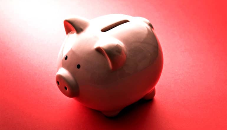 A piggy bank sits in a spotlight on a red surface