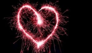 A pink sparkler makes the shape of a heart in the dark