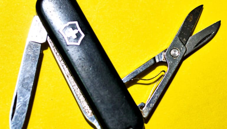 A black Swiss army knife open on a yellow background showing a knife and scissors