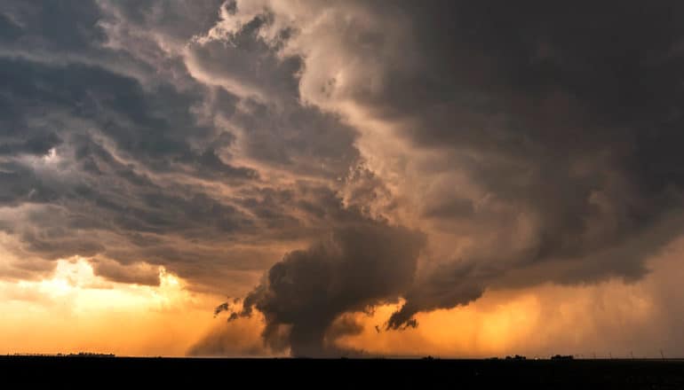 A massive dark cloud on the horizon with orange sunlight below it in the distance