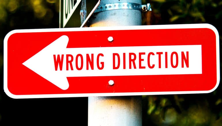 A red street sign with a white arrow reads "Wrong Direction"