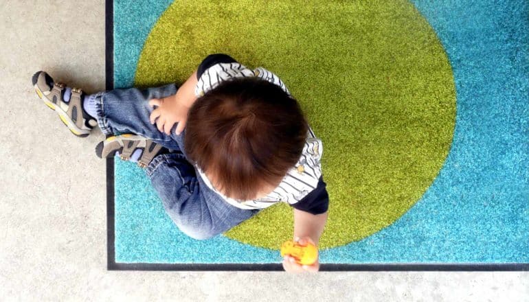 from above, baby sits holding toy