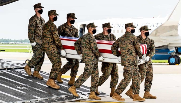 Marines carry a casket covered in an American flag off of a plane