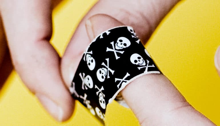 A person wraps a black bandaid covered in white skulls around their finger