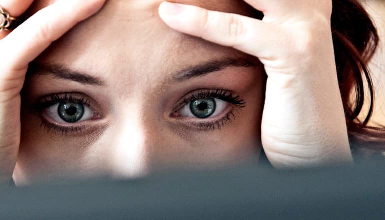 A woman holds her head in her hands while staring at a computer screen