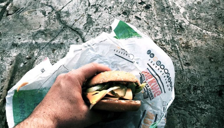 hand holds burger in paper wrapper on rock