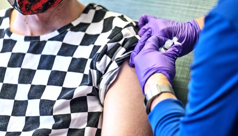 A person in a black and white checked t-shirt gets a COVID-19 vaccine shot