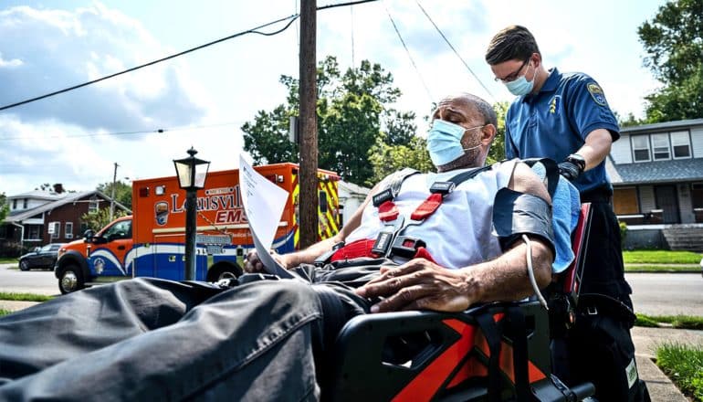 An EMS takes a man on a stretcher to a nearby ambulance