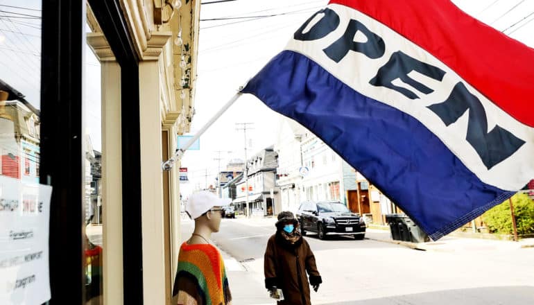 A person walks past a store wearing a face mask under a large flag that reads "OPEN"