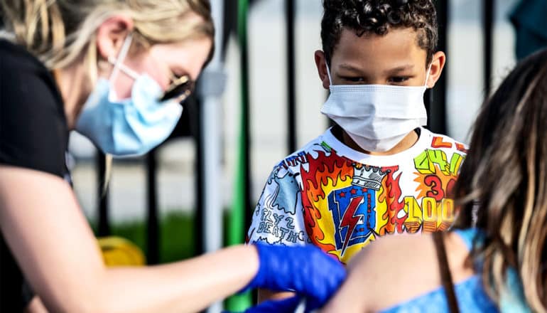 A kid watches a health worker give the COVID-19 vaccine to his mother