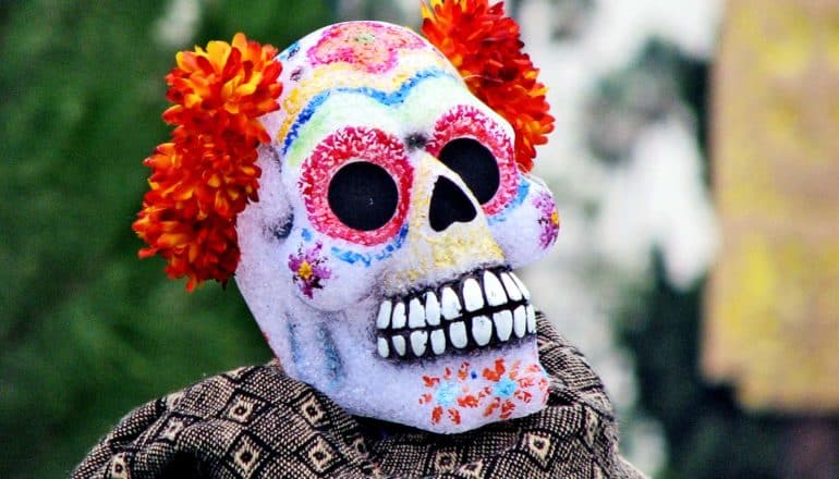 A colorfully painted sugar skull has a crown of orange and yellow flowers