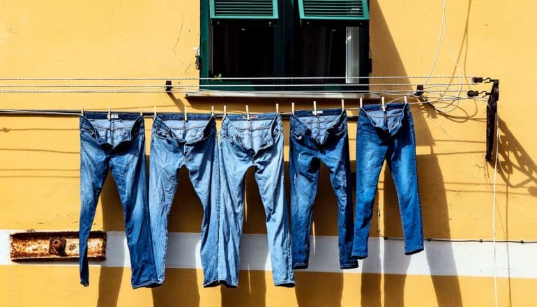 5 pairs of denim jeans hang on a clothesline outside a window in a yellow apartment building