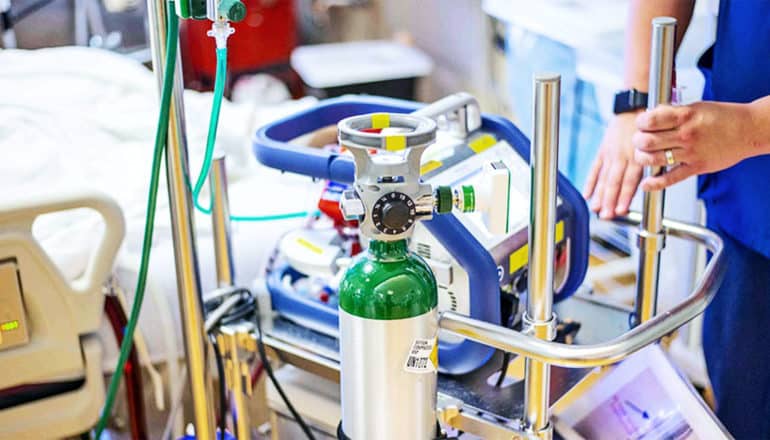 A health worker stands next to an ECMO life-support machine with an oxygen tank attached to it