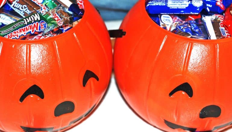 Two orange plastic jack-o-lanterns filled with Halloween candy