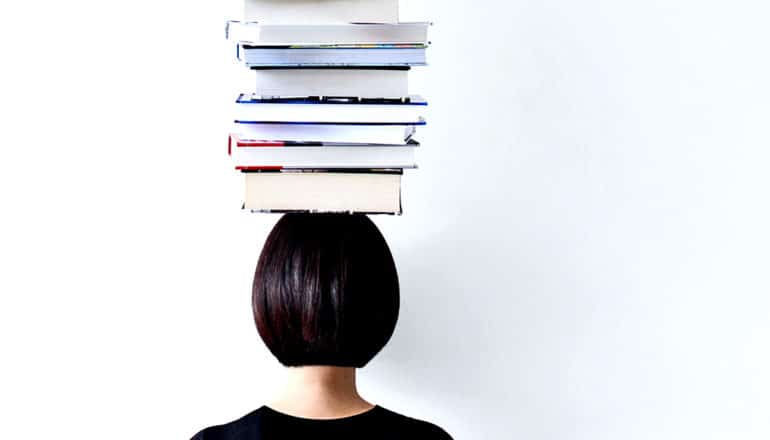 A young woman has a large number of books balanced on her head