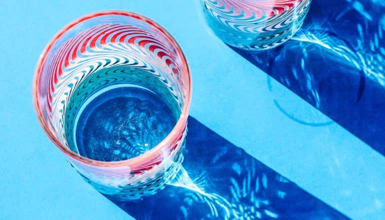 A colorful glass of water has light shining through it on a blue background