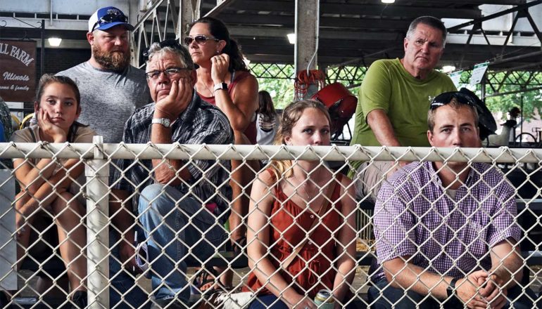 People at the iowa fair sit behind a chain link fence watching