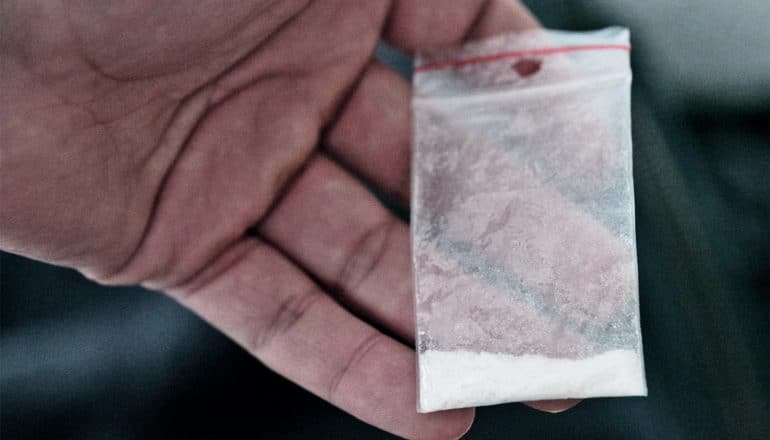 A man holds a small baggie with white powder in it