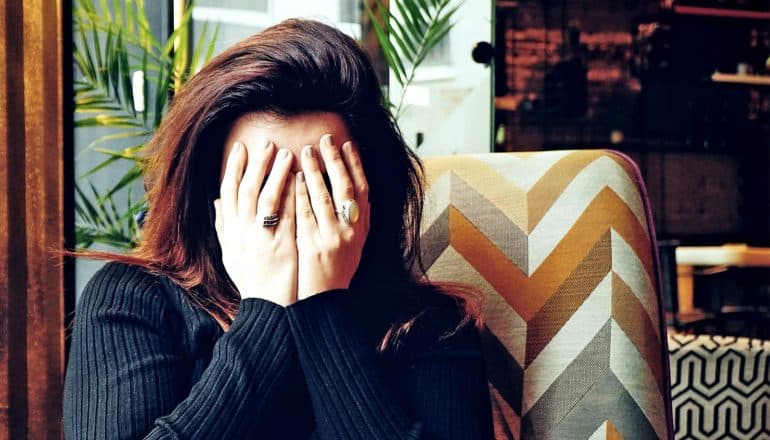 A woman sitting in a chair puts her hands over her face