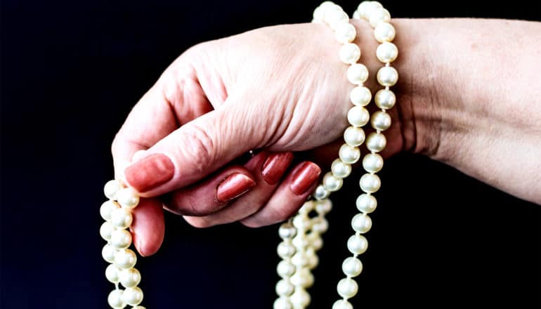 A woman dangles a pearl necklace draped around her hand