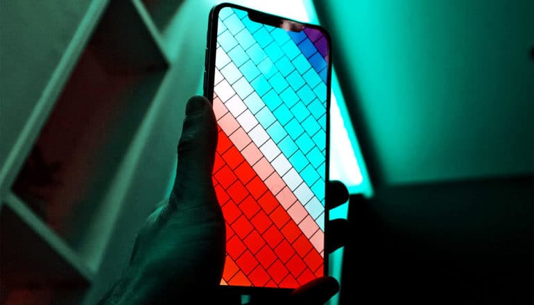 A person holds up a smartphone with a colorful mosaic background on the screen