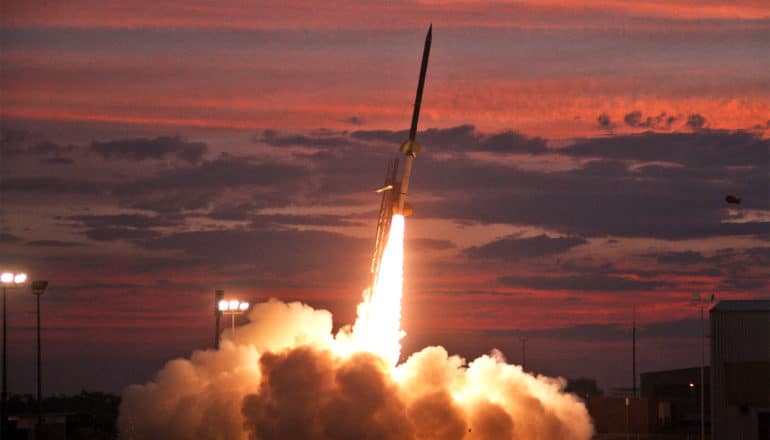 A rocket sprays fire as it lifts off against a red sky