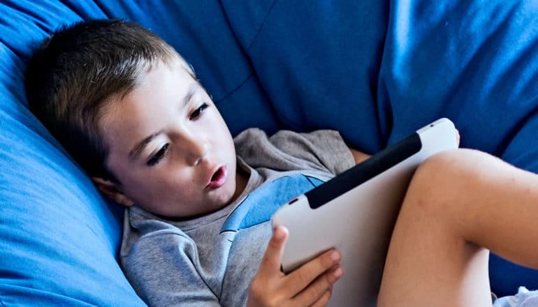 A young boy sitting on a blue bean bag chair watches an iPad