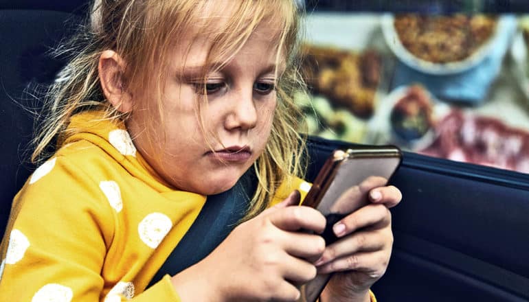 A young girl in a yellow hoodie holds a smart phone while in a car