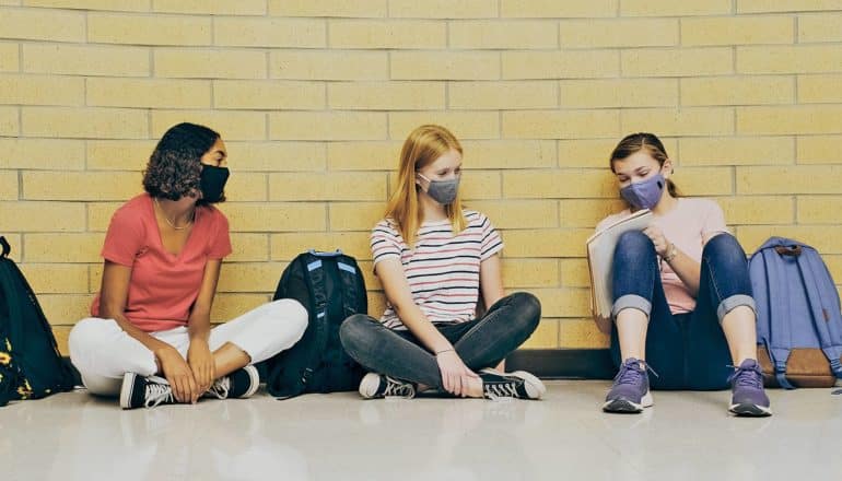 three teens sit in hallway looking at notebook