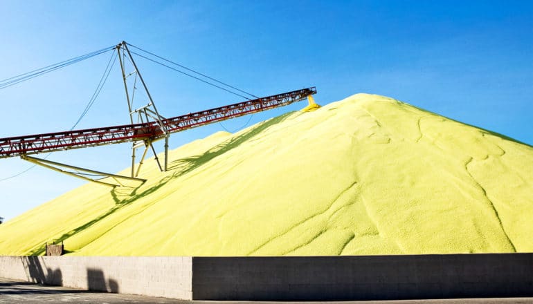 A massive pile of sulfur from a conveyer belt against a blue sky