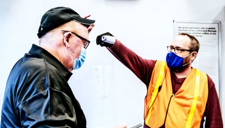 A store worker uses a thermometer gun to check another worker's temperature