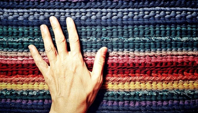 A person's hand touches a multi-colored woven fabric