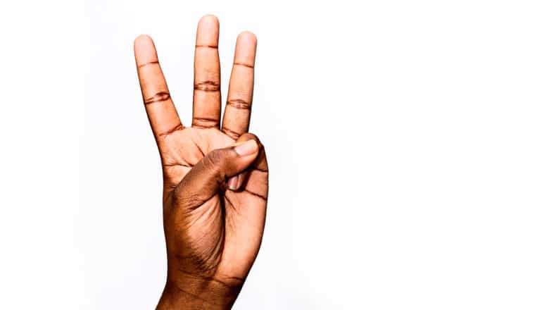 A woman's hand holding up the number 3 on a white background