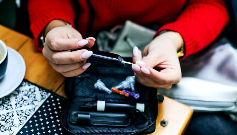 A woman in a red sweater sitting at a table checks her blood sugar