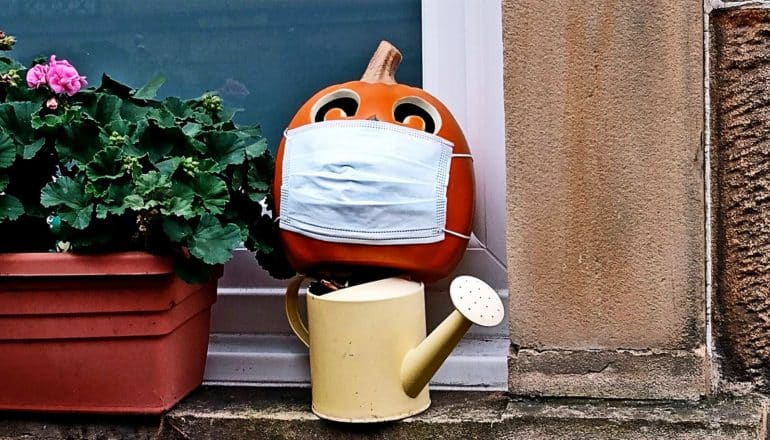 A jack-o-lantern on a porch has a face mask on it