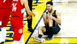 Klay Thompson holds his knee while sitting on the court and grimacing in pain