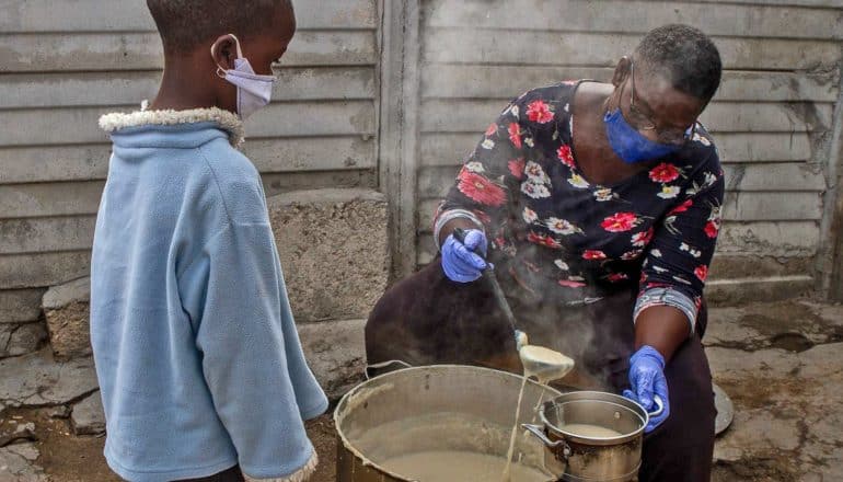 adult ladles porridge from pot for child in mask