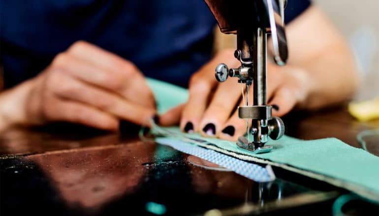 A person works at a sewing machine sewing blue fabric together