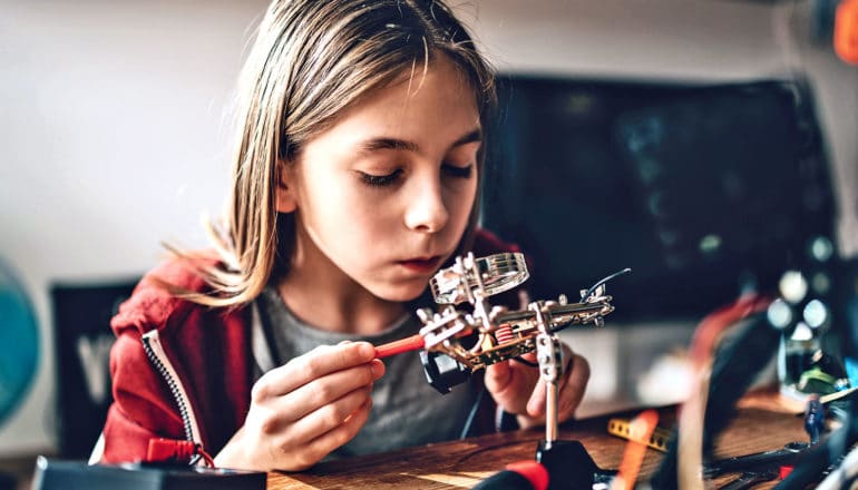 A young girl works on a circuit board at a desk