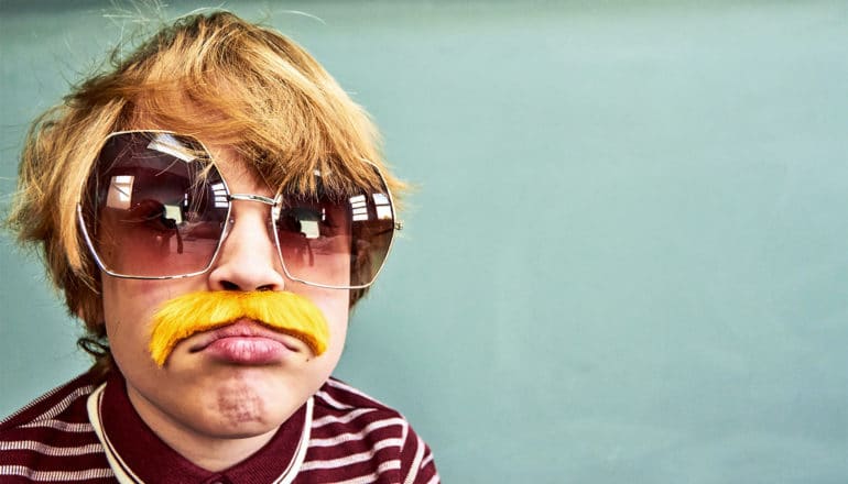 A young boy is dressed up as an older man with large sunglasses and a mustache