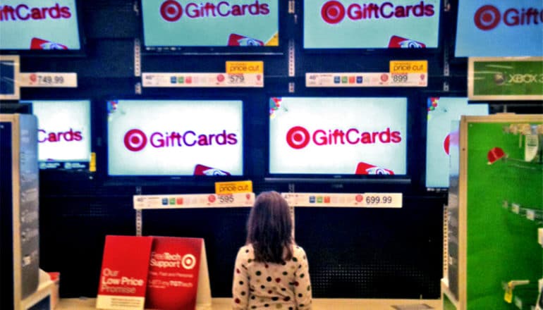 A young girl looks up at rows of televisions all displaying the phrase "Gift Cards"