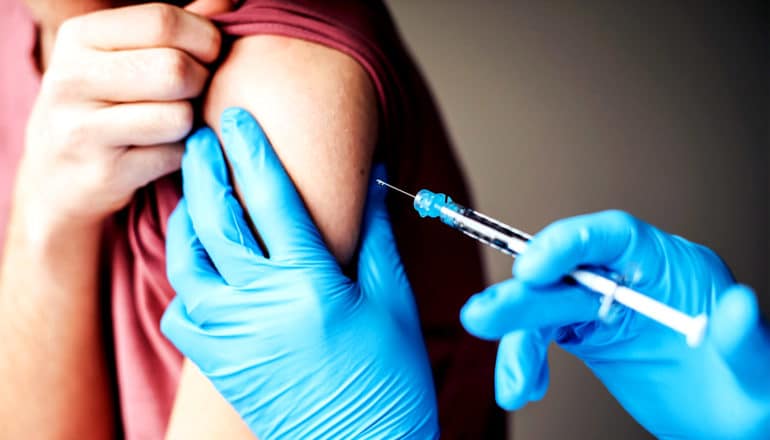 A young person gets a shot from a person wearing blue gloves