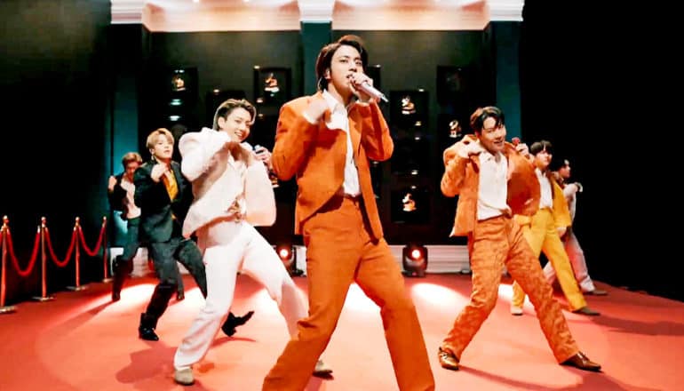 K-pop group BTS sing and dance in orange, white, and black suits at the Grammys