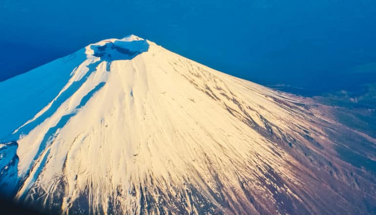 A snow-covered mountain shot from above with a shadowy crater at its peak